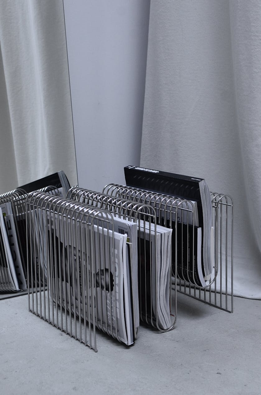 Collection of modern fashion magazines on metal rack placed on floor near mirror and curtain in room corner for a local press release
